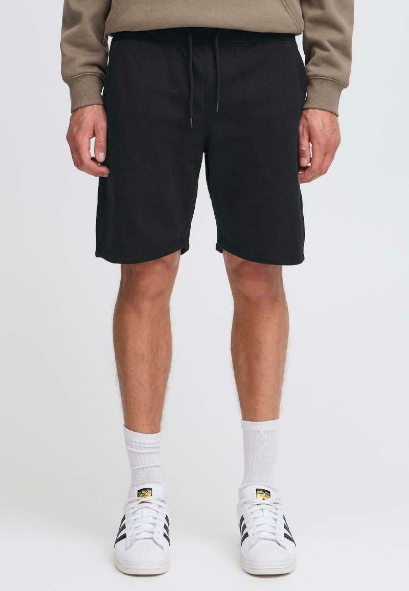 Shorts din bumbac negri, cu talie elastică reglabilă, buzunare laterale și croială confortabilă, asortați cu șosete albe și adidași clasici.
