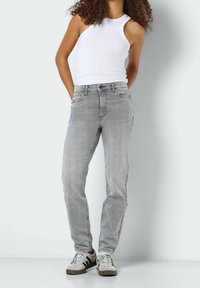 Jeans de mezclilla gris con un corte recto, cinco bolsillos y un ligero desgaste. Combinados con una camiseta sin mangas blanca y zapatillas claras.