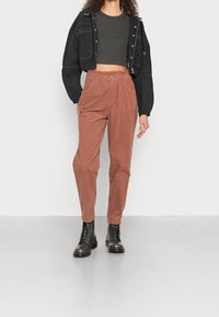 Černá zkrácená bunda s kapsami, v kombinaci s jemnými, rezavě zbarvenými, vysokými kordovými kalhotami a černými šněrovacími botami. Hladká textura.