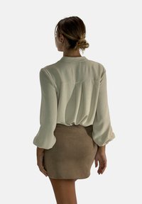 Lichtgroene blouse met volle mouwen, textuurstof en plooien aan de achterkant, gecombineerd met een tan gekleurde suède minirok.