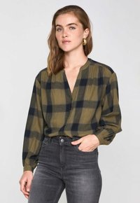 Grün und marineblau karierte Langarmbluse mit V-Ausschnitt, lockerer Passform und gerafften Ärmelbündchen, kombiniert mit dunkelgrauen Jeans.
