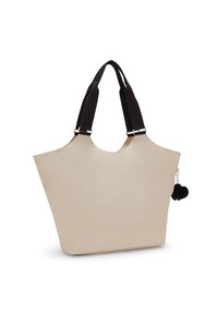 Beige tote bag with a unique shape, featuring black fabric handles and a decorative black pom-pom charm attached by a silver chain.