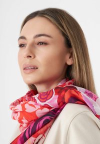 Écharpe florale dans des teintes de rouge, rose et violet. Tissu léger avec une texture lisse, présentant de grands motifs de roses. Portée lâchement autour du cou.