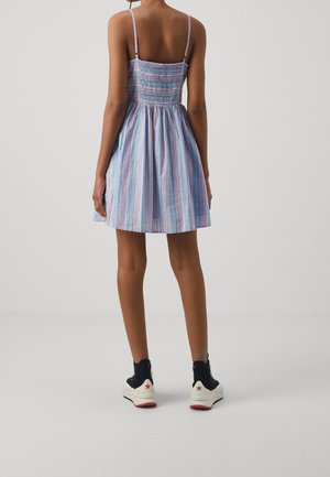 Robe à rayures bleues et roses avec un corsage smocké, une jupe évasée et des bretelles fines, associée à des baskets noires et blanches.