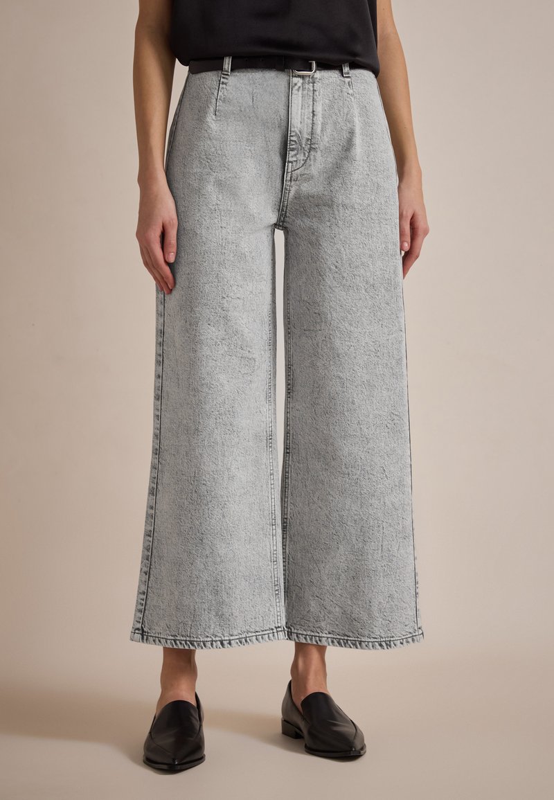 Vide ben med lys grå denim med en frynset kant, med høyt liv og en ren finish. Sammen med svarte sko.