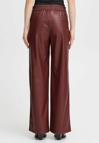 Bordeaux faux leren wijde broek met een elastische tailleband, een gladde textuur en een losse pasvorm, eindigend boven zwarte hakken.