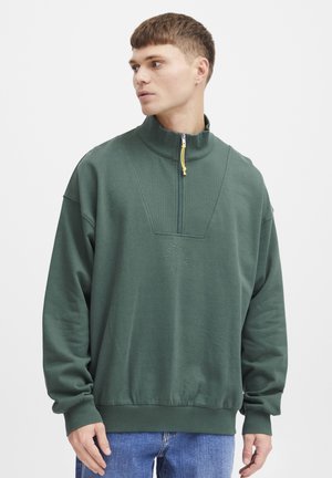 Grønn zip-up hettegenser med høy krage, teksturert frontpanel, ribbestrikkede mansjetter og hem, med et sirkulært logodetalj på brystet.