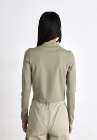 Long-sleeve top in soft olive green fabric with a high neck. Features a fitted design and smooth texture, paired with light beige trousers.