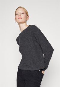 Sudadera gris de manga larga en una tela suave y texturizada, con cuello redondo y un corte ligeramente holgado, combinada con pantalones negros.