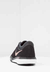 Musta urheilukenkä, jossa on verkkopinta, harmaat yksityiskohdat ja vaaleanpunainen Nike-logo. Pyöristetty kanta ja valkoinen pohja. Tekstuuri on sileä ja hengittävä materiaali.