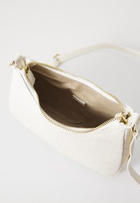 Borsa bianca con texture, dotata di una cerniera e un manico dorati. L'interno è foderato in beige liscio e presenta una piccola etichetta all'interno.