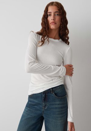 Witte katoenen blouse met lange mouwen en een ronde hals, gecombineerd met donkerblauwe denim jeans. Heeft een getailleerde snit en een gladde textuur.