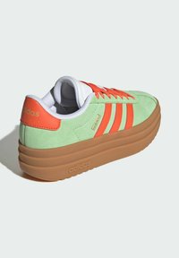 Zelena nubuk tenisica s narančastim detaljima, bijelim vezicama i smešim platforma potplatom. Tri narančaste pruge i logo na peti.
