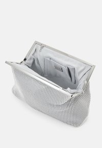 Pochette à perles argentées avec un cadre métallique. L'intérieur est doublé d'un tissu gris clair et comprend une petite poche. Forme arrondie et douce.