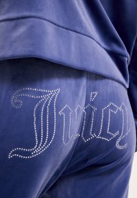 Niebieskie welurowe spodnie dresowe z napisem "Juicy" wykonanym z dżetów na tyle. Gładka faktura i dopasowany krój.