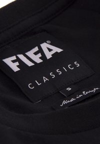 Etichetta in tessuto nera con "FIFA CLASSICS" in carattere bianco grande, taglia "S," e la scritta "Made in Europe." Texture liscia con bordi cuciti.
