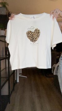 Baltā īsā krekla ar mīkstu audumu dizains, kas satur leopardu rakstu sirdī, ar melnu tekstu "Manas sirds ir savvaļa". Brīvā piegriezuma.