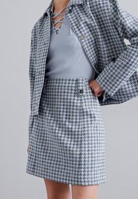 Svetlomodrá súprava so vzorom houndstooth, ktorá pozostáva z sakového kabátu s gombíkmi a priliehavého mini sukne s jemnou textúrou a detailmi.