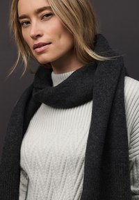 Sciarpa in lana nera avvolta intorno al collo, abbinata a un maglione chiaro grigio a coste con motivo a diamante testurizzato.