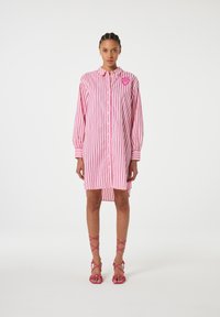 Rosa und weiß gestreiftes Hemdkleid mit Knopfverschluss, langen Ärmeln und abgerundetem Saum. Verfügt über ein Herzlogo auf der Brust.
