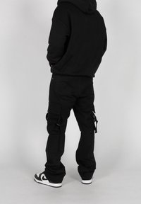 Black hooded sweatshirt with a relaxed fit paired with black cargo pants featuring side pockets and strap details. White sneakers complete the look.