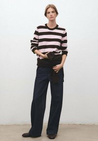 Suéter a rayas negro y rosa con mangas largas, combinado con jeans de mezclilla oscuros de pierna ancha y cintura alta. Suéter oscuro atado a la cintura.