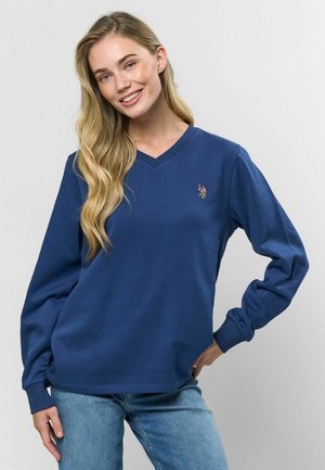 Sweatshirt bleumarin cu mânecă lungă și decolteu în V, cu manșete și tiv striate. Prezintă un mic logo brodat pe pieptul stâng. Textură de material neted.