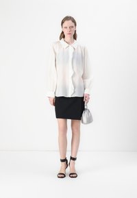 Blusa leggera e trasparente bianca con maniche a palloncino e chiusura a bottoni, abbinata a una gonna nera aderente e una borsa argento. Sandali neri con tacco.