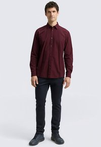 Camicia bordeaux con bottoni e motivo a trama, maniche lunghe e collo classico, abbinata a pantaloni slim fit scuri e scarpe nere.