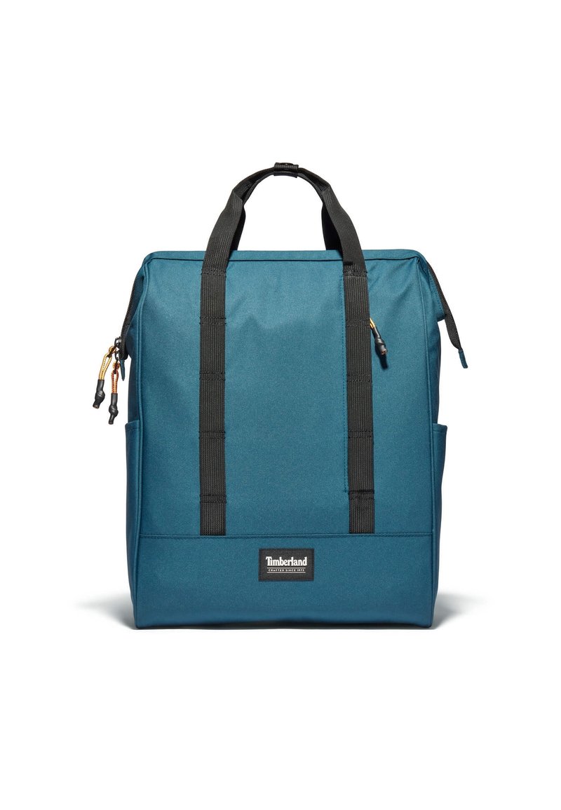 Blå tygryggsäck med svarta remmar och detaljer. Har en logotyp patch, dragkedjestängning och sidofickor för extra förvaring.