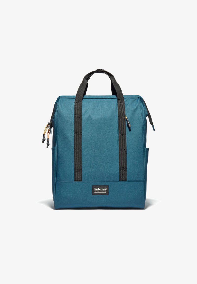 Blå tygryggsäck med svarta remmar och detaljer. Har en logotyp patch, dragkedjestängning och sidofickor för extra förvaring.