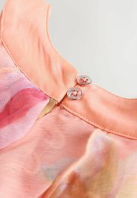 Rosa geblümtes Kleid mit rundem Kragen, verziert mit glänzenden Knöpfen und zartem Stofftextur. Nahtdetails sind am Hals zu sehen.