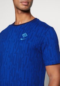 Modrý sportovní tričko vyrobené z texturované látky, s kulatým výstřihem, pruhovaným vzorem a decentními brandingovými akcenty ve světlé modré.