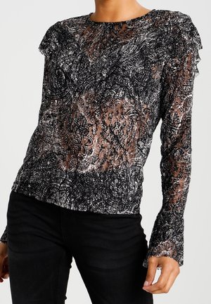 Haut transparent noir et gris à manches longues avec des motifs tourbillonnants complexes, porté avec un pantalon noir, ajusté sur une personne montrée du cou aux hanches.