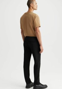 Khaki krótki rękaw t-shirt zestawiony z czarnymi spodniami, charakteryzujący się luźnym krojem i teksturowanym materiałem. Czarny obuwie dopełnia stylizację.