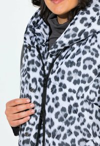 Gilet imbottito con una stampa leopardata bianca e nera, chiusura a zip frontale, cappuccio oversize e bottoni automatici sul colletto. Tessuto liscio e lucido.
