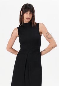 Black sleeveless dress with a high neckline, structured bodice, and pleated skirt. Smooth texture and tailored fit, minimalist design.