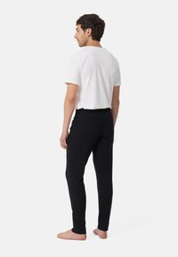 Schwarze Hose mit tailliertem Design, aus weichem Material hergestellt, mit einem Bund und glatter Textur, kombiniert mit einem schlichten weißen T-Shirt.