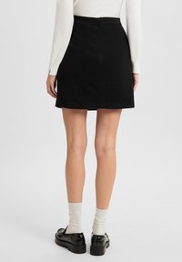 Schwarzer A-Linien-Rock mit glatter Textur, mit einem Reißverschluss auf der Rückseite. Kombiniert mit klobigen schwarzen Schuhen und weißen gerippten Socken.