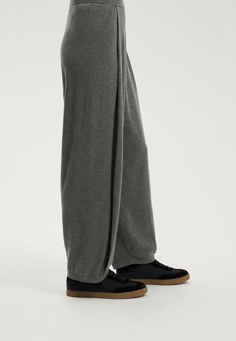 Gray wide-leg sweatpants made of soft fabric, featuring a relaxed fit and accented by a black sneaker with a gum sole.