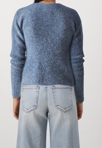 Blauer Wollpullover mit strukturiertem Finish, Rundhalsausschnitt und langen Ärmeln, kombiniert mit hellblauen Denim-Jeans mit Gesäßtaschen.