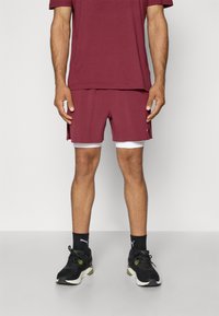 Shorts bordeaux avec un contour blanc, associés à une chemise assortie. Comprend une coupe décontractée et athlétique, portés avec des baskets noires.