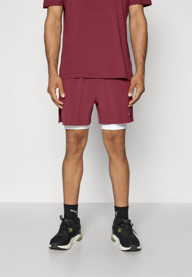 Shorts bordeaux avec un contour blanc, associés à une chemise assortie. Comprend une coupe décontractée et athlétique, portés avec des baskets noires.