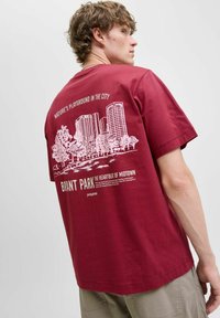 Bordeaux bomulds t-shirt med et hvidt grafisk print af bygninger og træer på ryggen, med tekst om BNYMT Park i fed skrift. Korte ærmer.