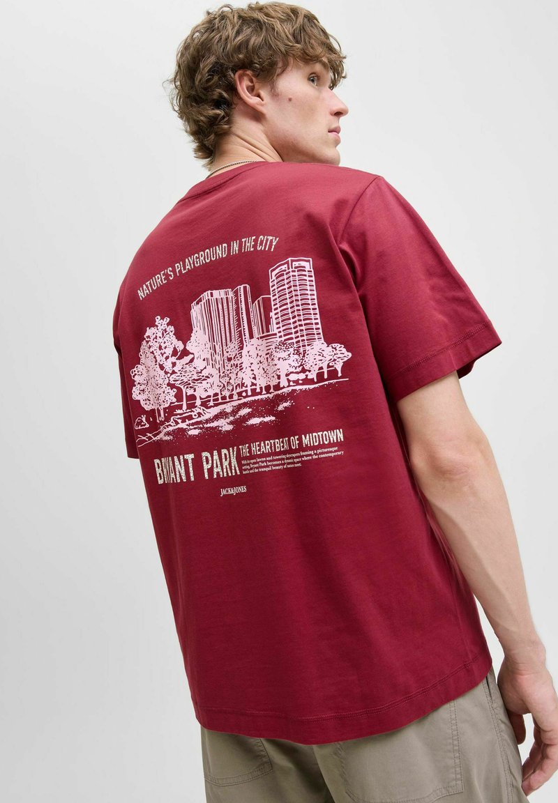 Bordeaux bomulds t-shirt med et hvidt grafisk print af bygninger og træer på ryggen, med tekst om BNYMT Park i fed skrift. Korte ærmer.