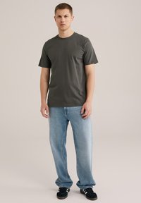Mörkgrå bomulls T-shirt med rund halsringning och korta ärmar, tillsammans med ljusblå denimjeans. Sneakers med svarta och vita detaljer.