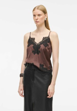 Camisole en satin marron avec des bordures en dentelle noire à l'encolure et à l'ourlet, fines bretelles réglables. Portée avec une jupe en cuir taille haute.