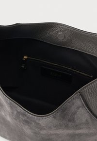 Interior de geantă din piele intoarsă gri și piele neagră, cu căptușeală din țesătură neagră și un buzunar interior cu fermoar auriu.