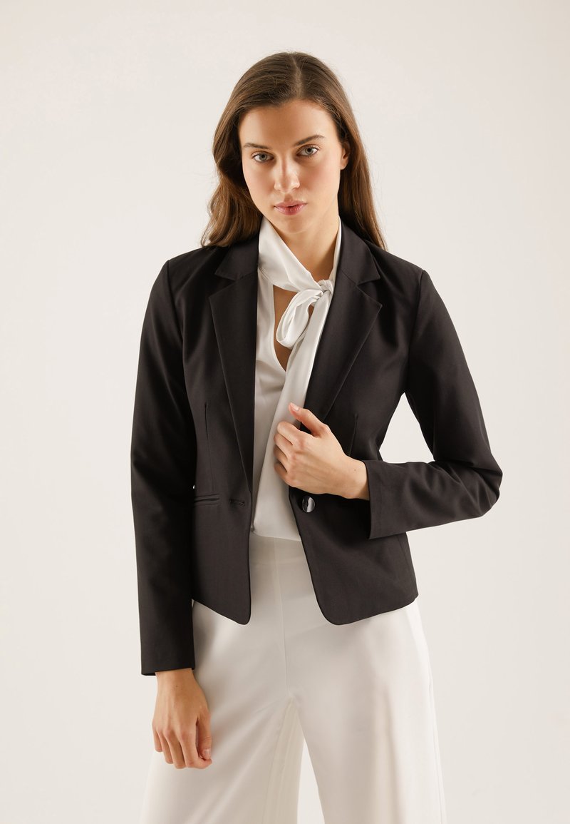 Schwarzer taillierter Blazer aus glattem Stoff mit Reverskragen, einer Knopfverschluss und dezenten Taschen, kombiniert mit einer weißen Bluse.
