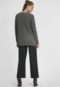 Gray textured knit sweater with a round neckline paired with black wide-leg trousers and heeled boots. The outfit features a relaxed fit.